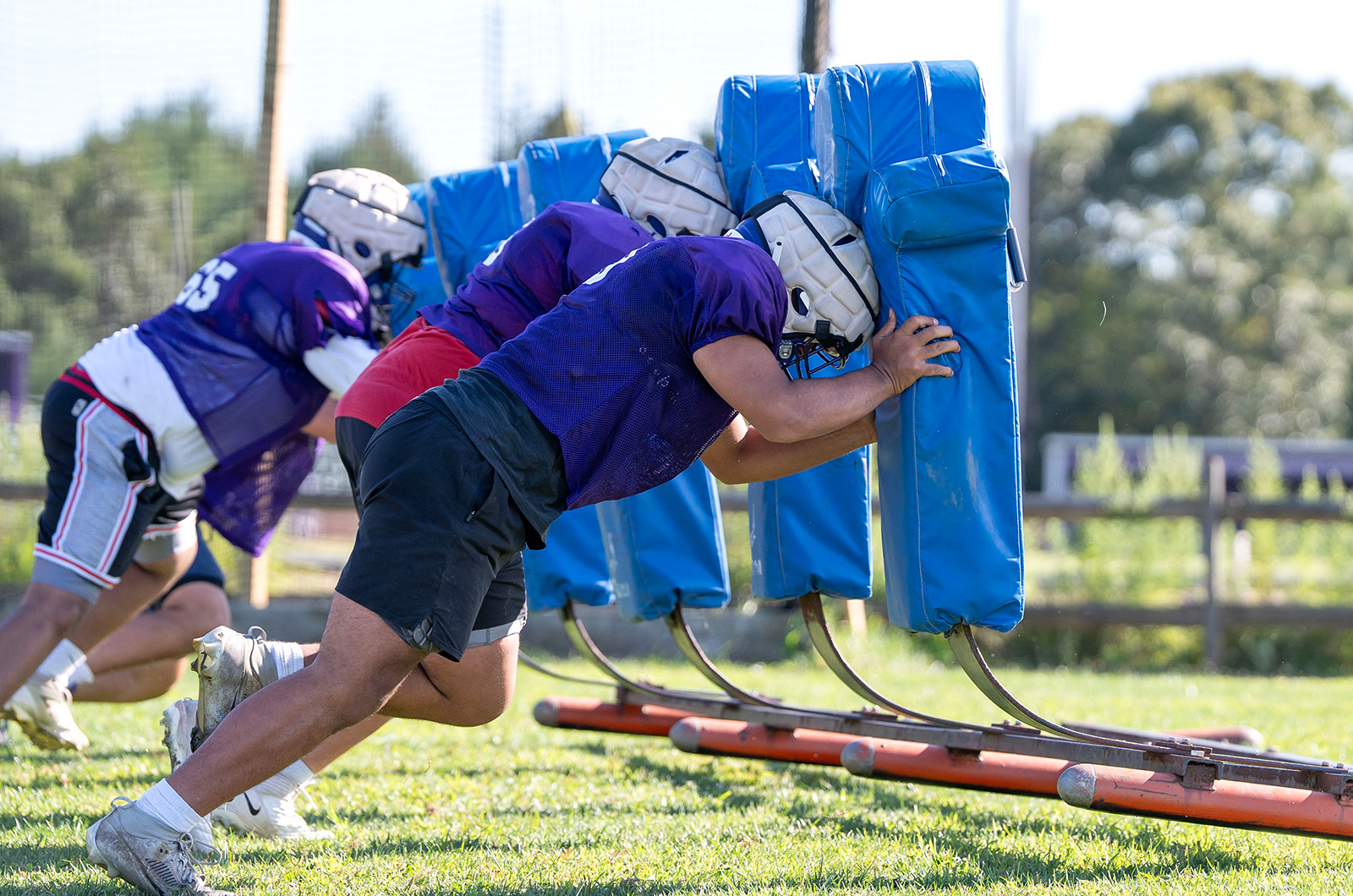 Football players line up and hit the sleds.