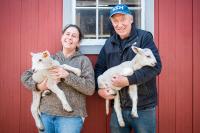 Christa and Arnie Fischer of Flat Point Farm holding lambs by their barn.